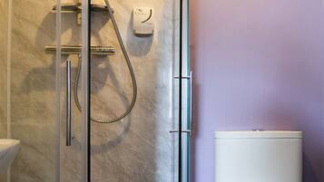 Un baño con ducha de vidrio, inodoro blanco y pared de mármol.