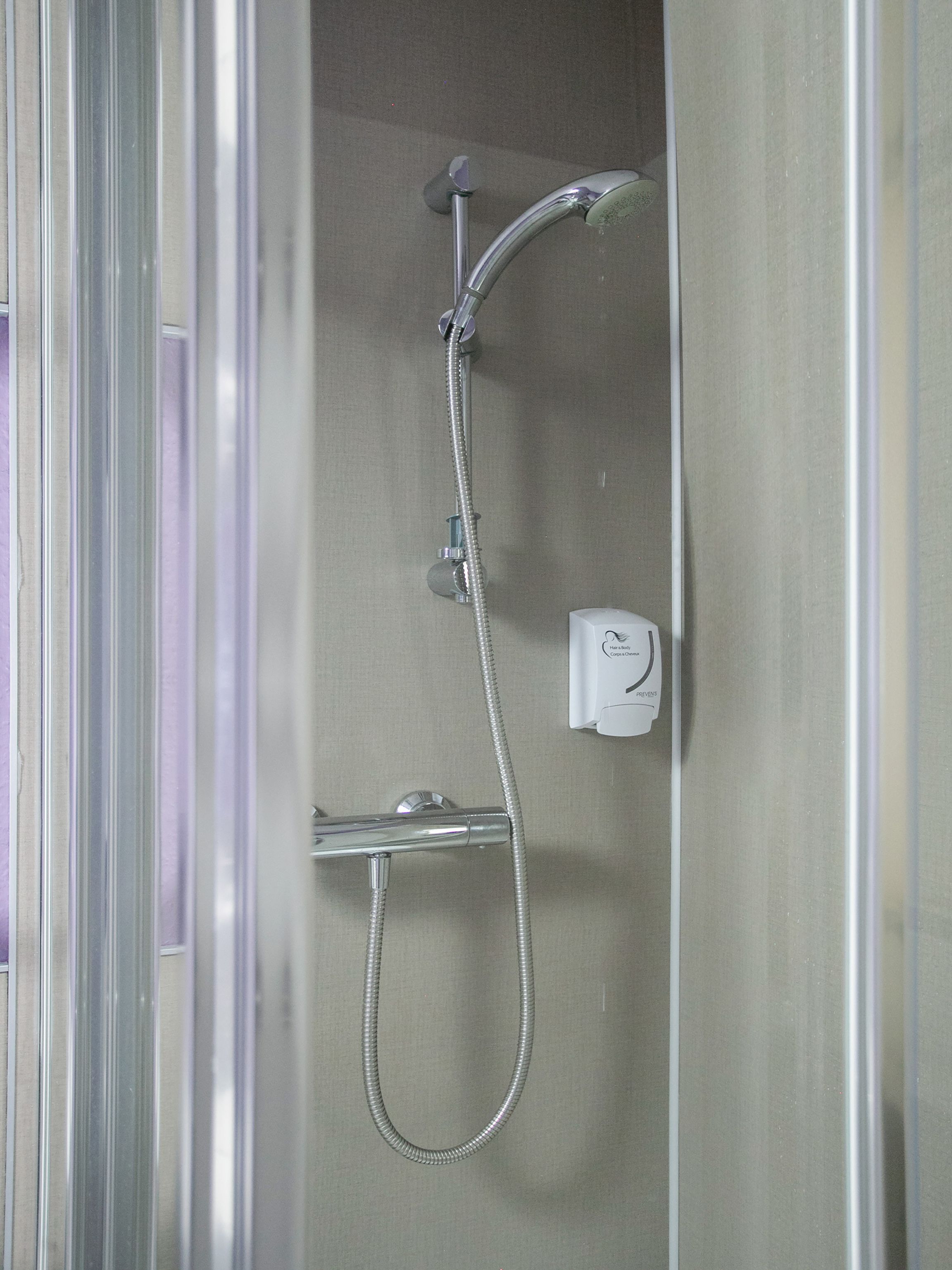 A shower with a handheld hose and a wall-mounted control panel.