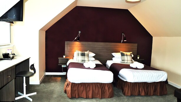 A modern hotel room with two beds, a desk, and a chair.