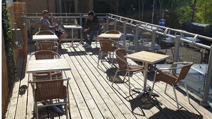 A wooden deck with tables and chairs, a railing, and a view of parked cars.