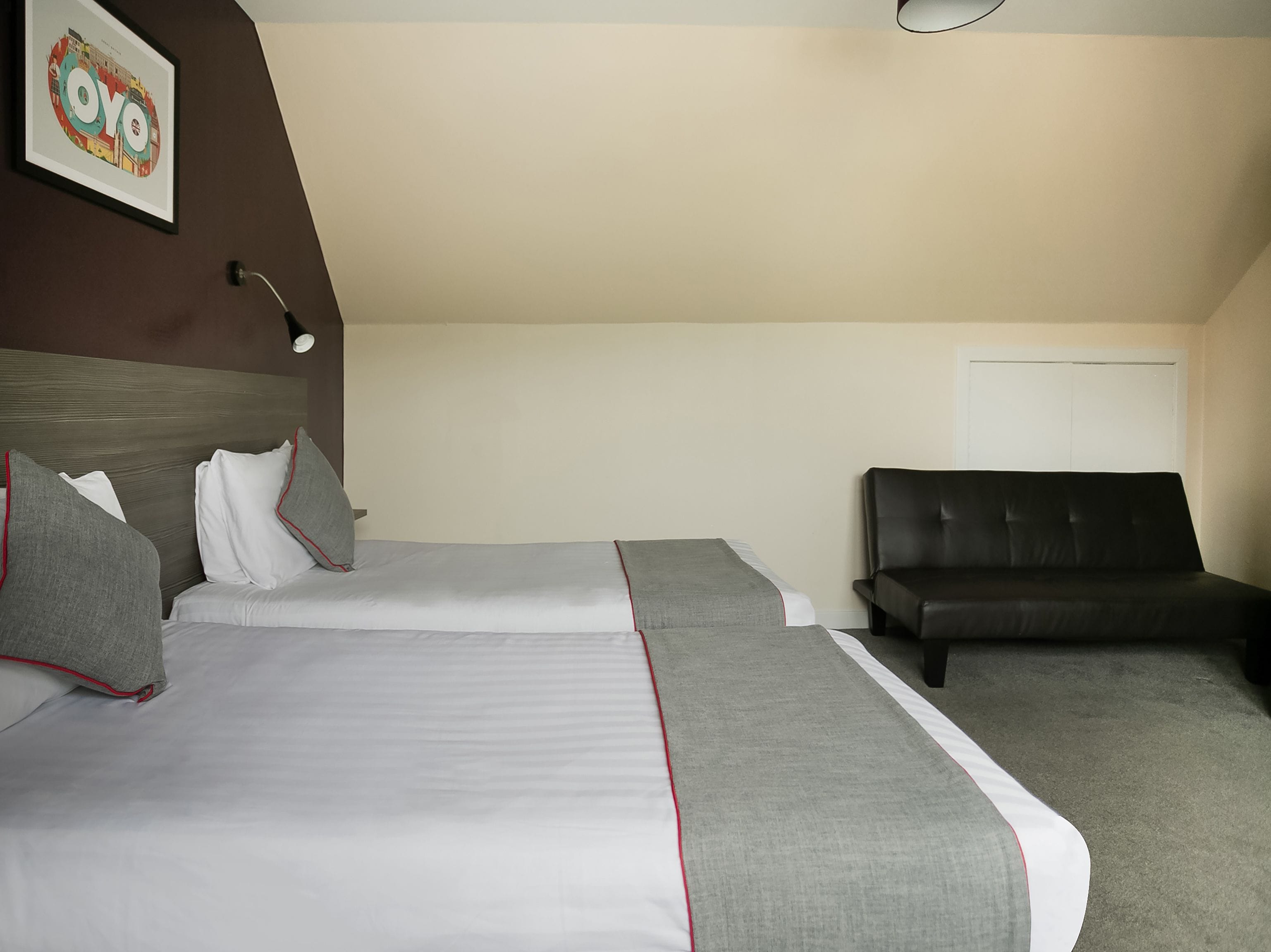 Habitación de hotel con dos camas, un sofá, una lámpara de pared y una puerta.