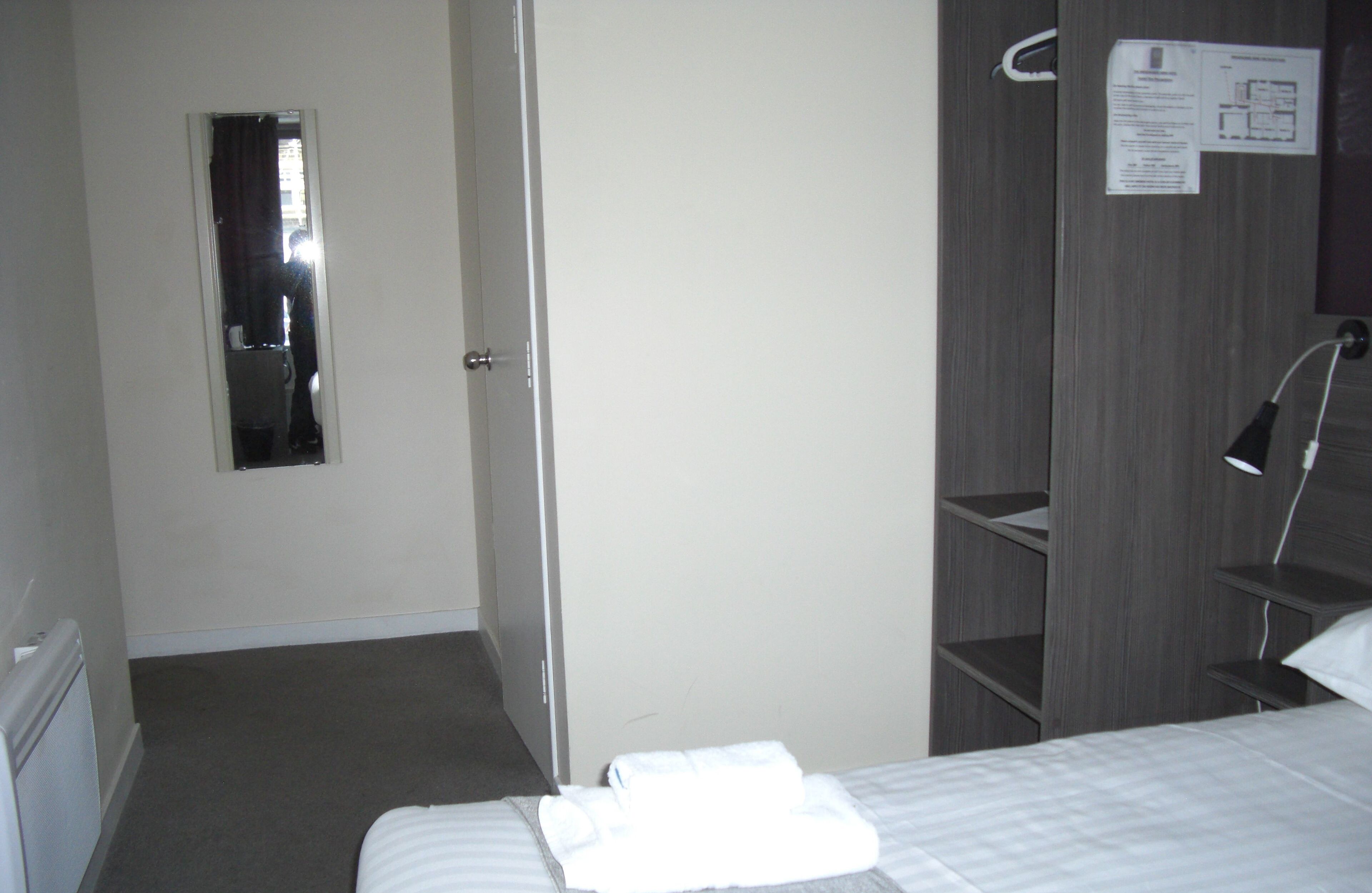 A hotel room with a bed, a mirror, a door, and a wardrobe.