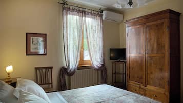 Un dormitorio con una cama, un armario de madera, un televisor sobre un mueble, una silla y una ventana con cortinas.