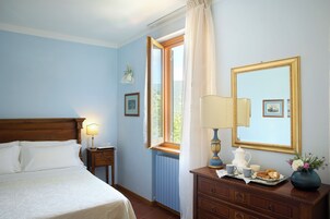 A bedroom with a bed, bedside table, lamp, dresser, mirror, and window with curtains.