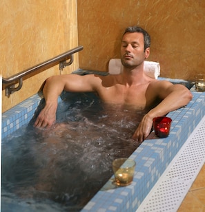 Une personne se détend dans une baignoire, avec une serviette et une bougie.