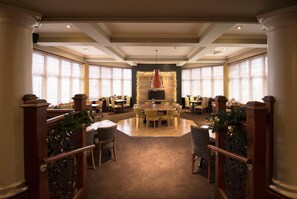 A spacious dining area with a central round table surrounded by chairs, flanked by large windows with blinds. - Premier Inn Glasgow - Motherwell (Motherwell)