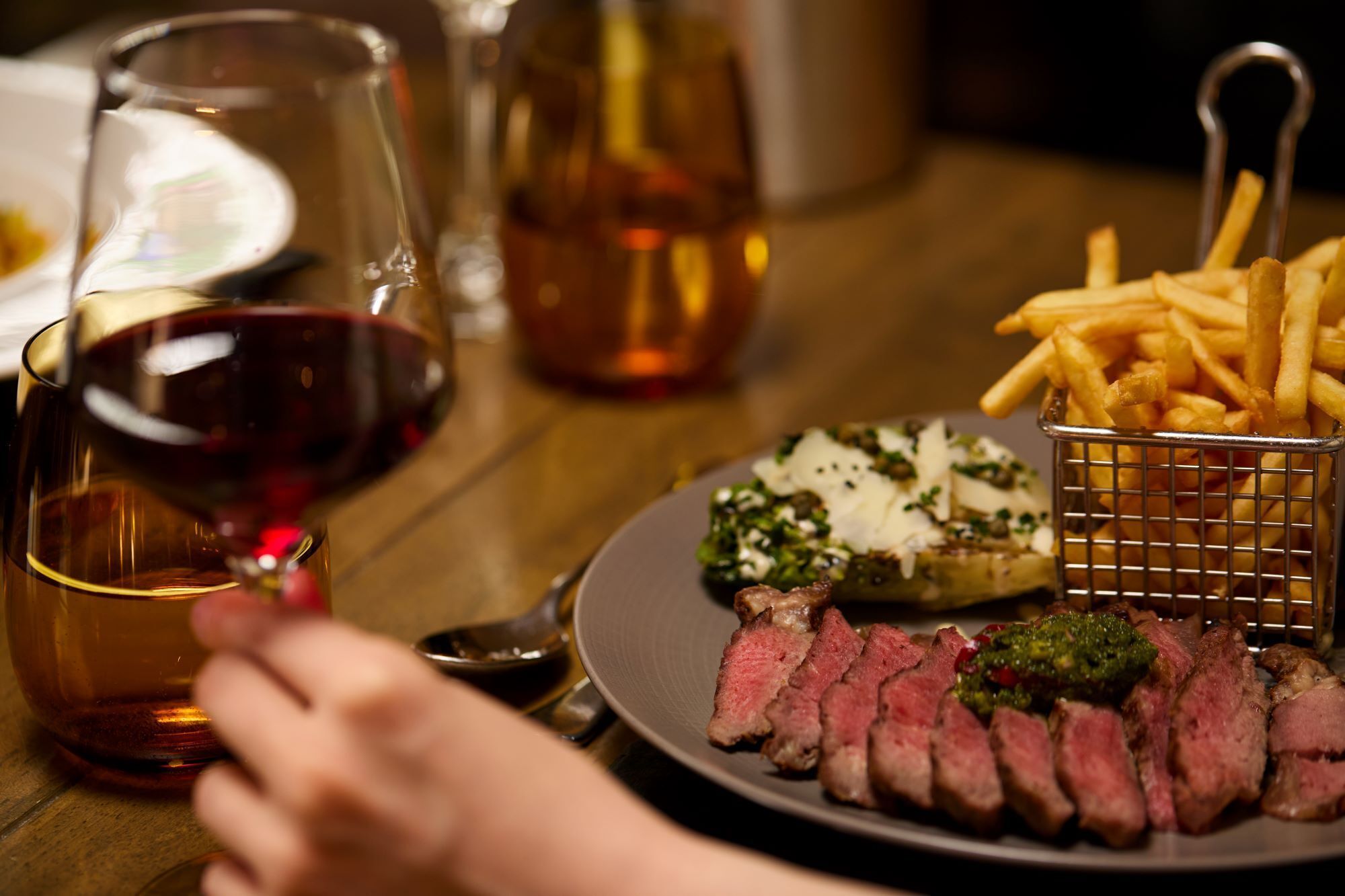 A plate of sliced steak with a side of fries and a glass of red wine.