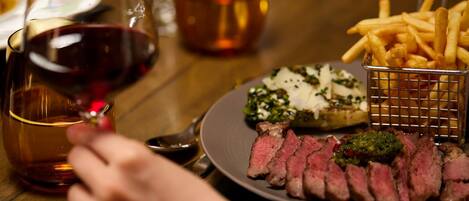 A plate of sliced steak with a side of fries and a glass of red wine.