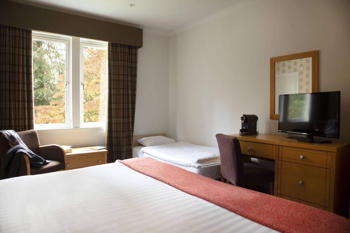 A hotel room with a large bed, a desk with a television, a chair, and a window with curtains.