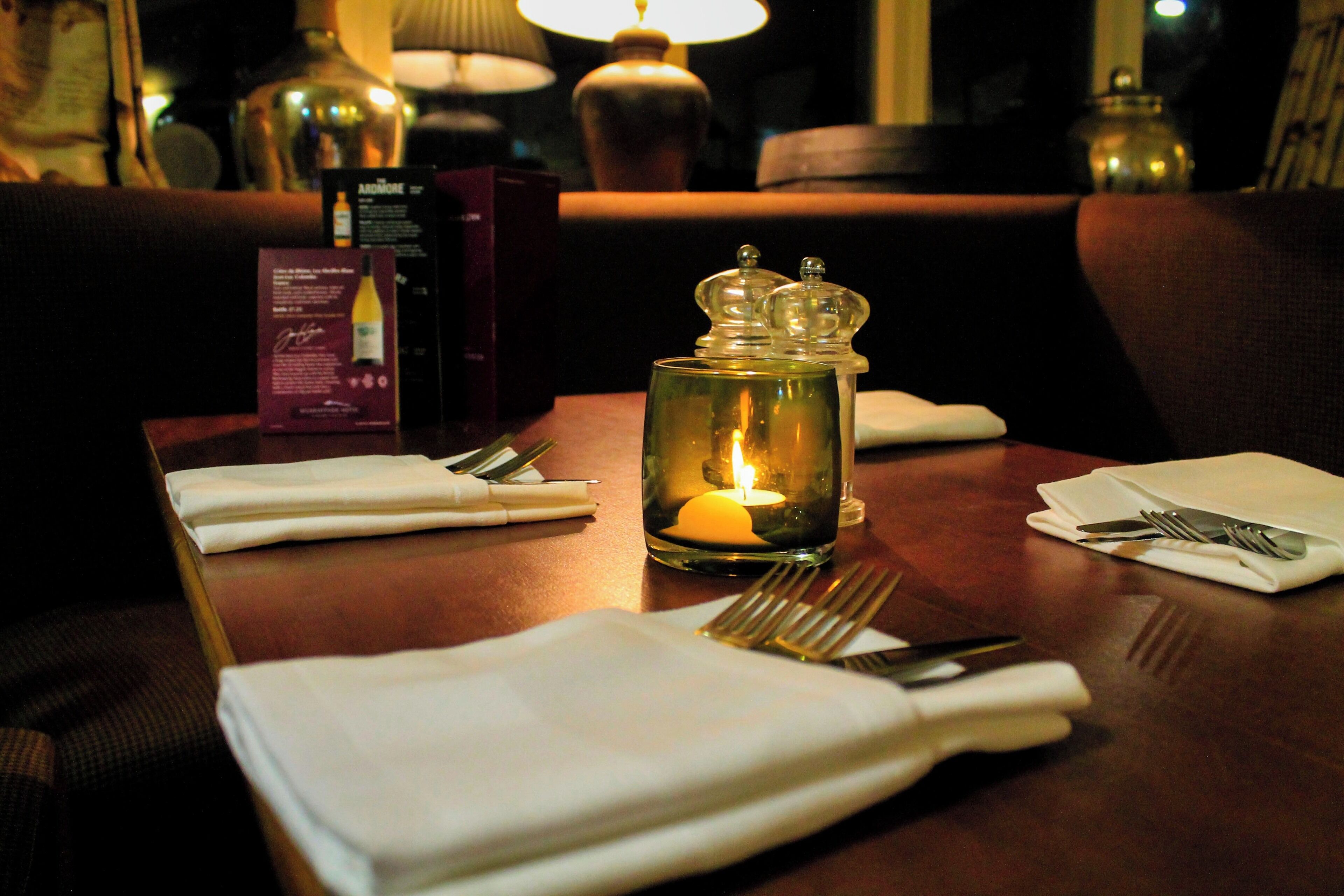 Una mesa de comedor dispuesta con servilletas blancas, cubiertos y una vela encendida en un frasco de vidrio.