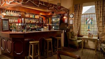 Un espace bar doté de tabourets en bois, d’une variété de bouteilles d’alcool et d’un élément décoratif en forme de bois de cerf placé au-dessus du bar.