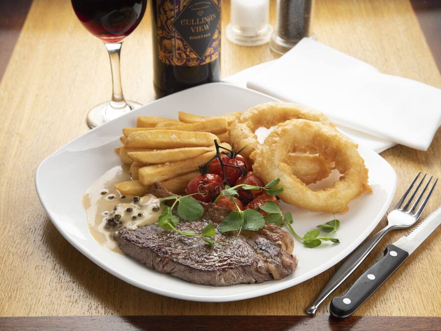 Un plato de comida con bistec, papas fritas, aros de cebolla y una bebida.