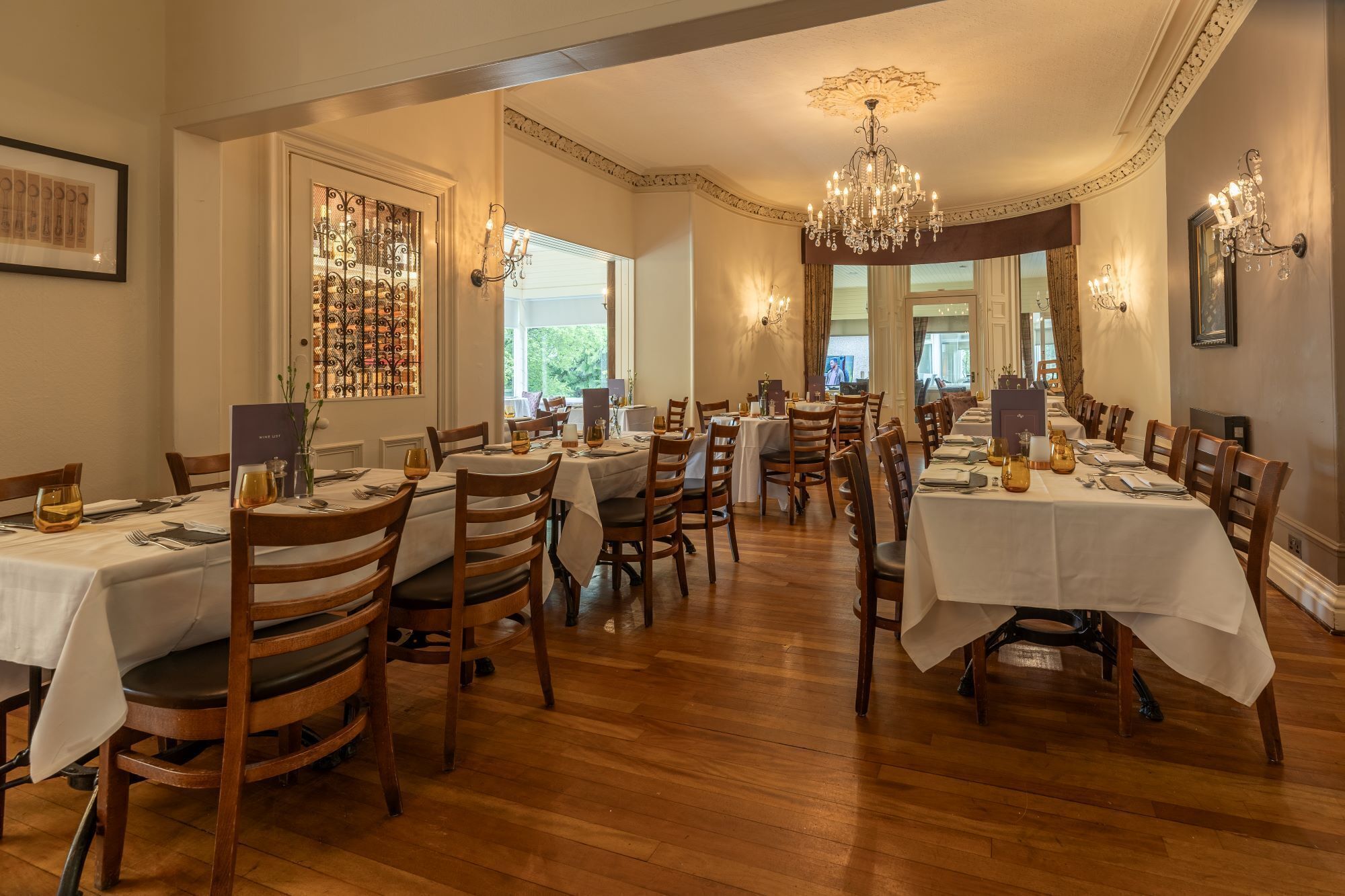 A dining area with multiple tables and chairs, a chandelier, and a large window with a view.