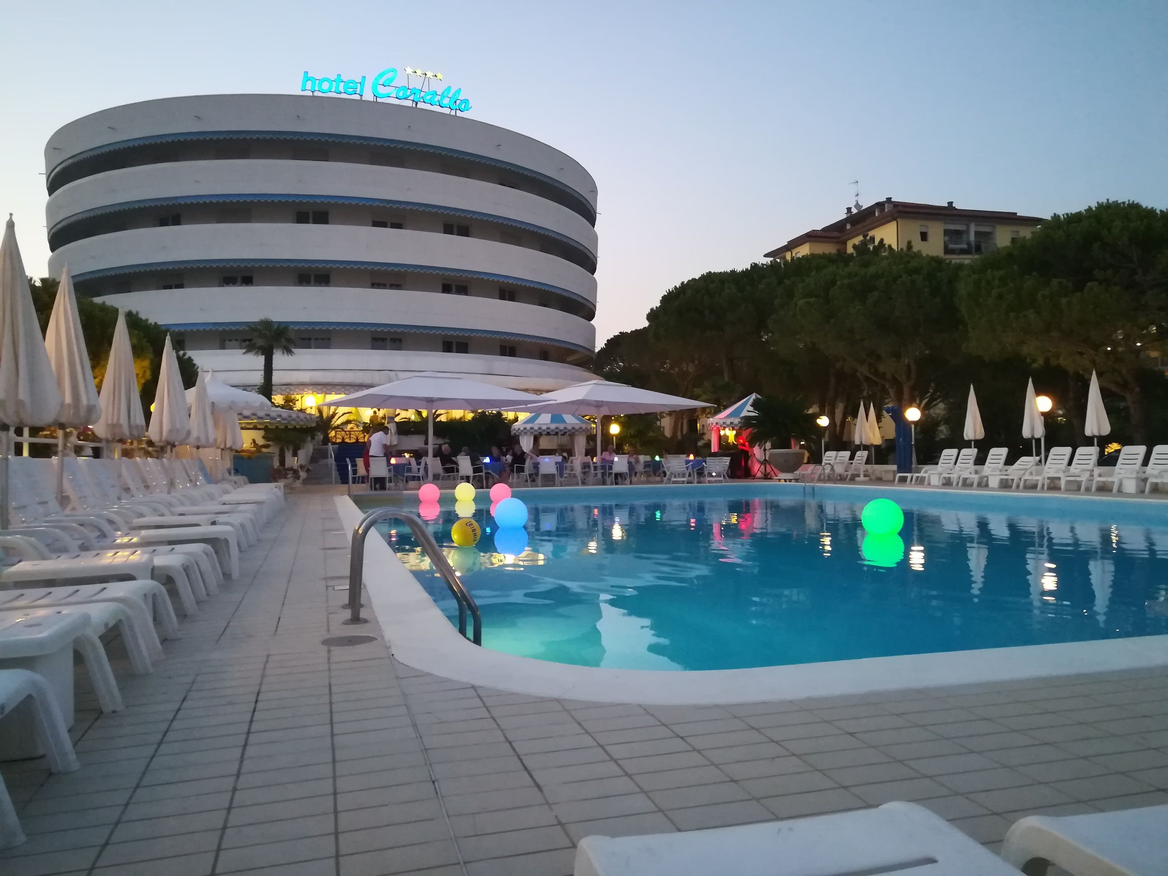 Una piscina con lettini, ombrelloni e un cartello con la scritta 'hotel Corallo'.