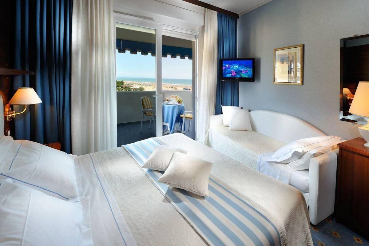 Une chambre d’hôtel avec deux lits, une télévision, un balcon avec une table et une chaise, et vue sur la plage.