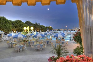 An outdoor pool area with umbrellas and chairs, surrounded by greenery and a clear sky. - Hotel Corallo (San Michele al Tagliamento)