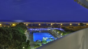 Ein Nachtblick auf einen Resort mit großem Pool, Strandstühlen und einem gut beleuchteten Strand.