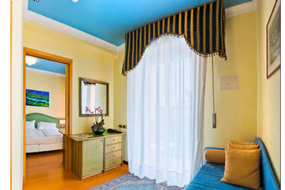 A bedroom with a bed, a dresser, a mirror, and a window with curtains.