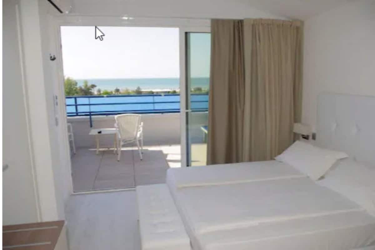 A hotel room with a bed, a chair, and a view of the sea through a balcony.