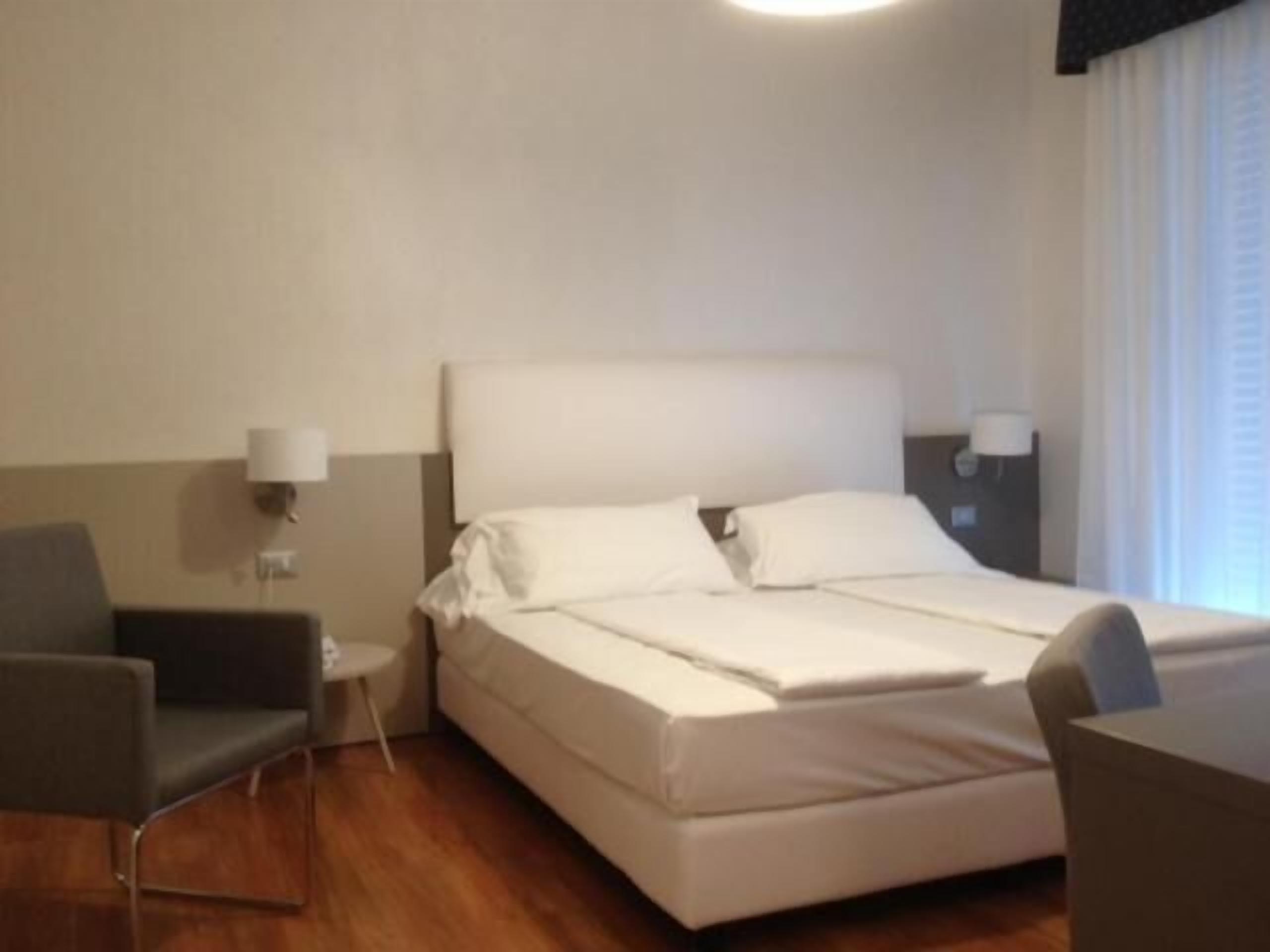 Una habitación de hotel con una cama, una silla, una mesita y una lámpara.