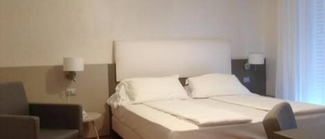 Una habitación de hotel con una cama, una silla, una mesita y una lámpara.