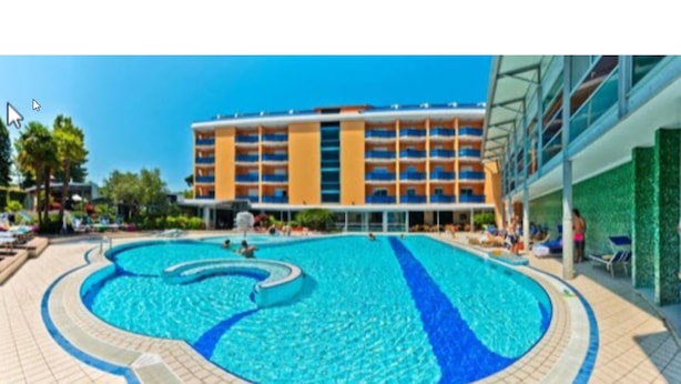 A hotel with a large swimming pool, a multi-story building with balconies, and a clear blue sky.