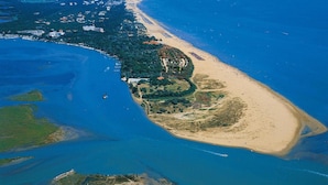 An aerial view of a coastal area with a beach, a marina, and a dense cluster of buildings along the shore.