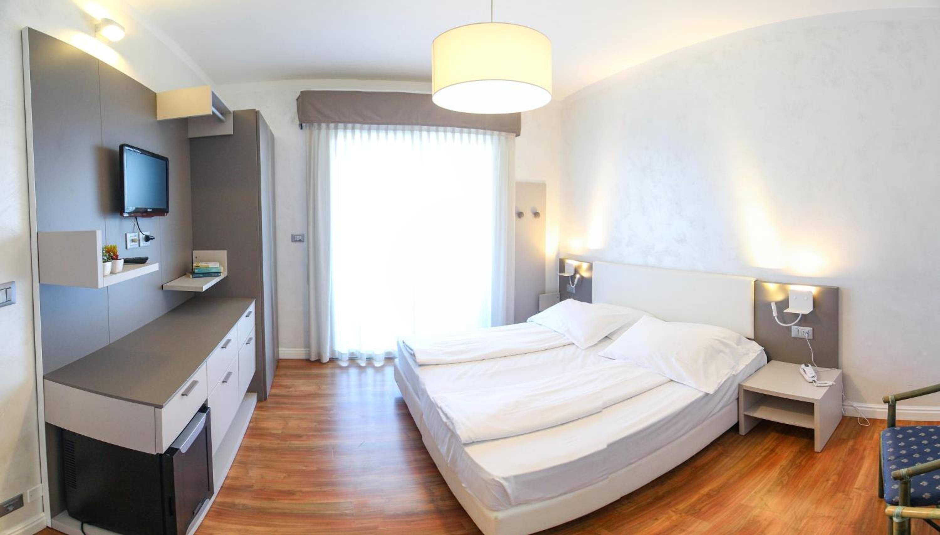 Une chambre d’hôtel moderne équipée d’un lit, de tables de chevet, d’une télévision et d’un bureau avec une chaise.
