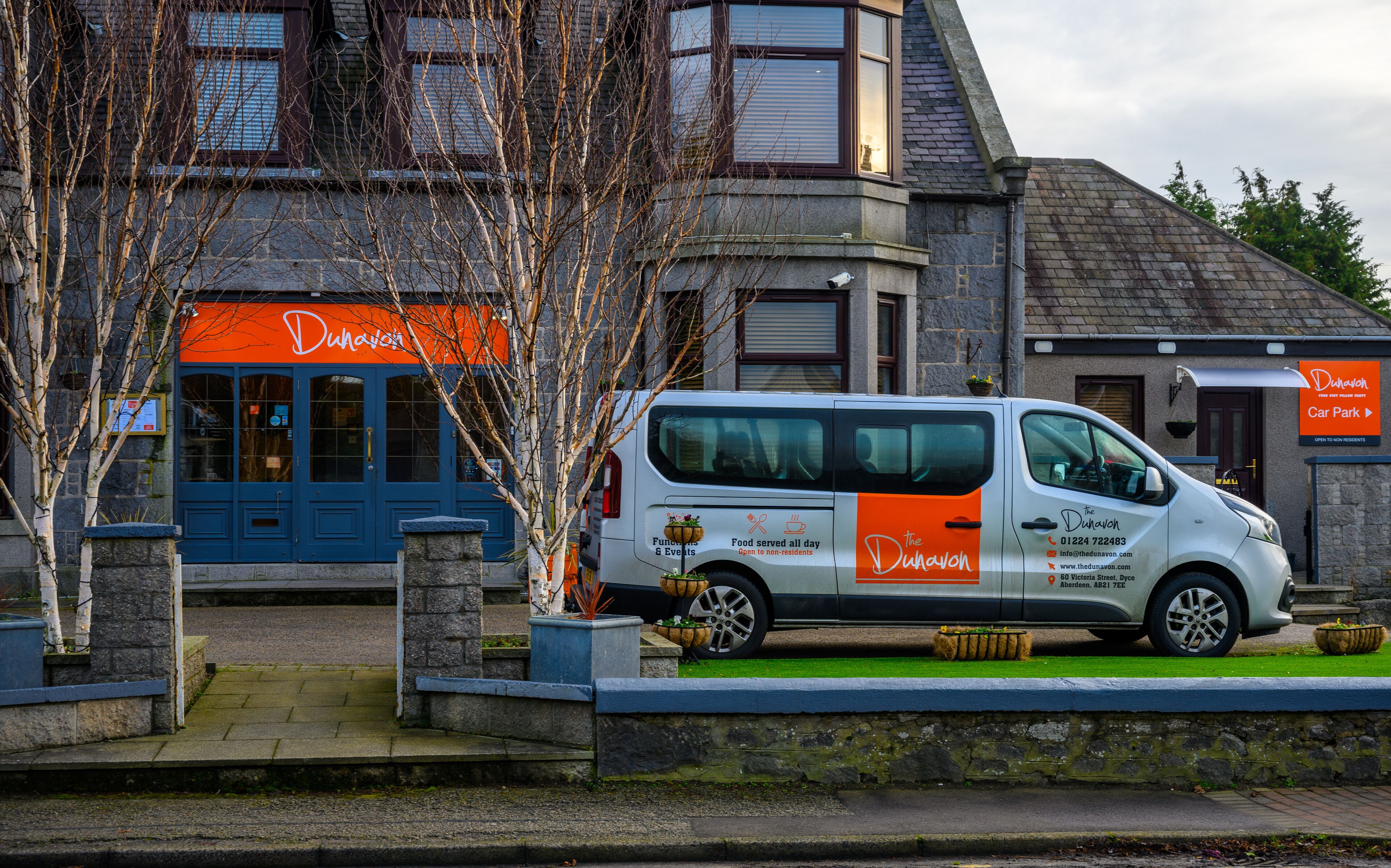 Un fourgon blanc était garé devant un immeuble dont la porte était bleue et qui affichait une enseigne orange sur laquelle on pouvait lire « Dunavon ».