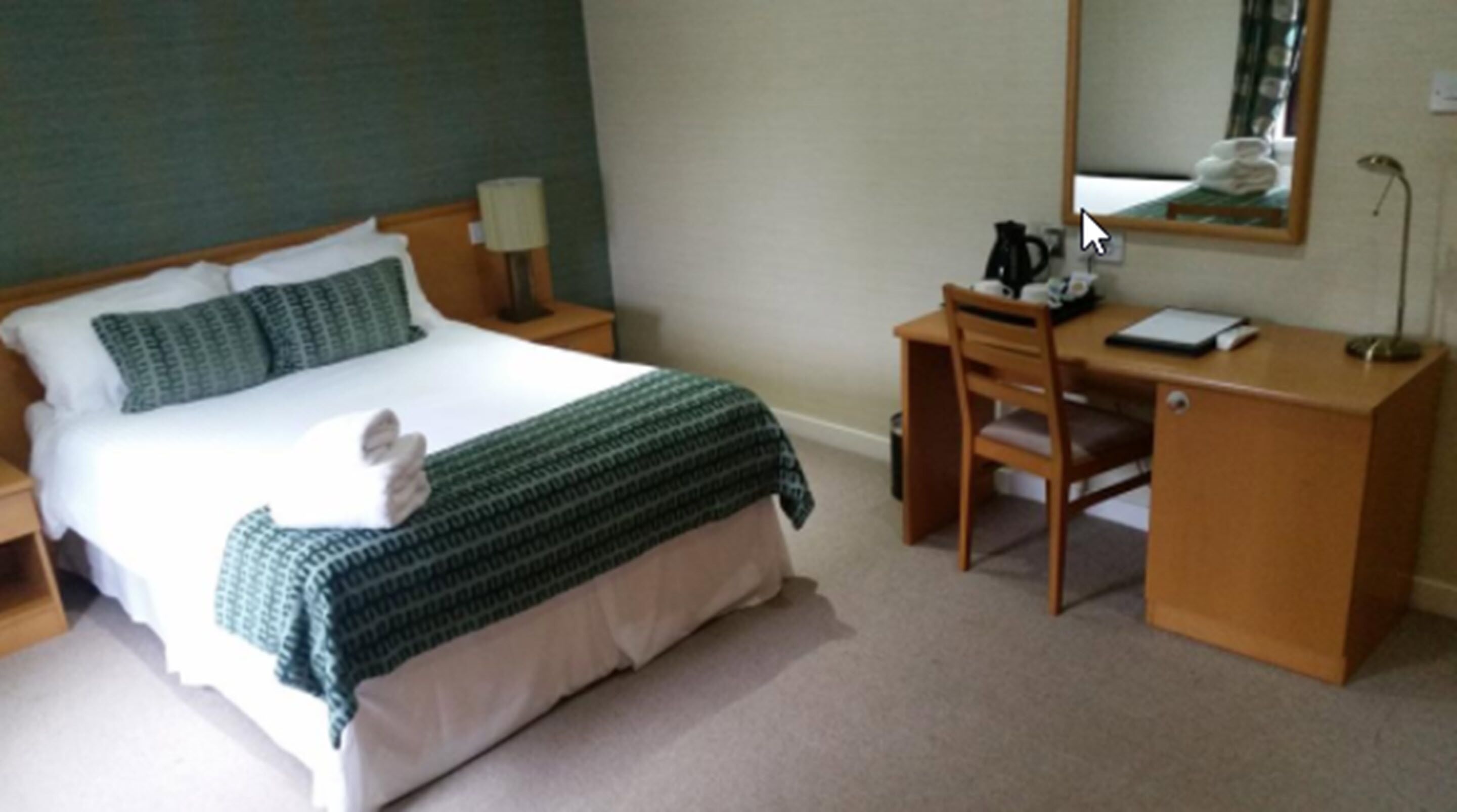 Una habitación de hotel con cama, escritorio, silla, lámpara y espejo.