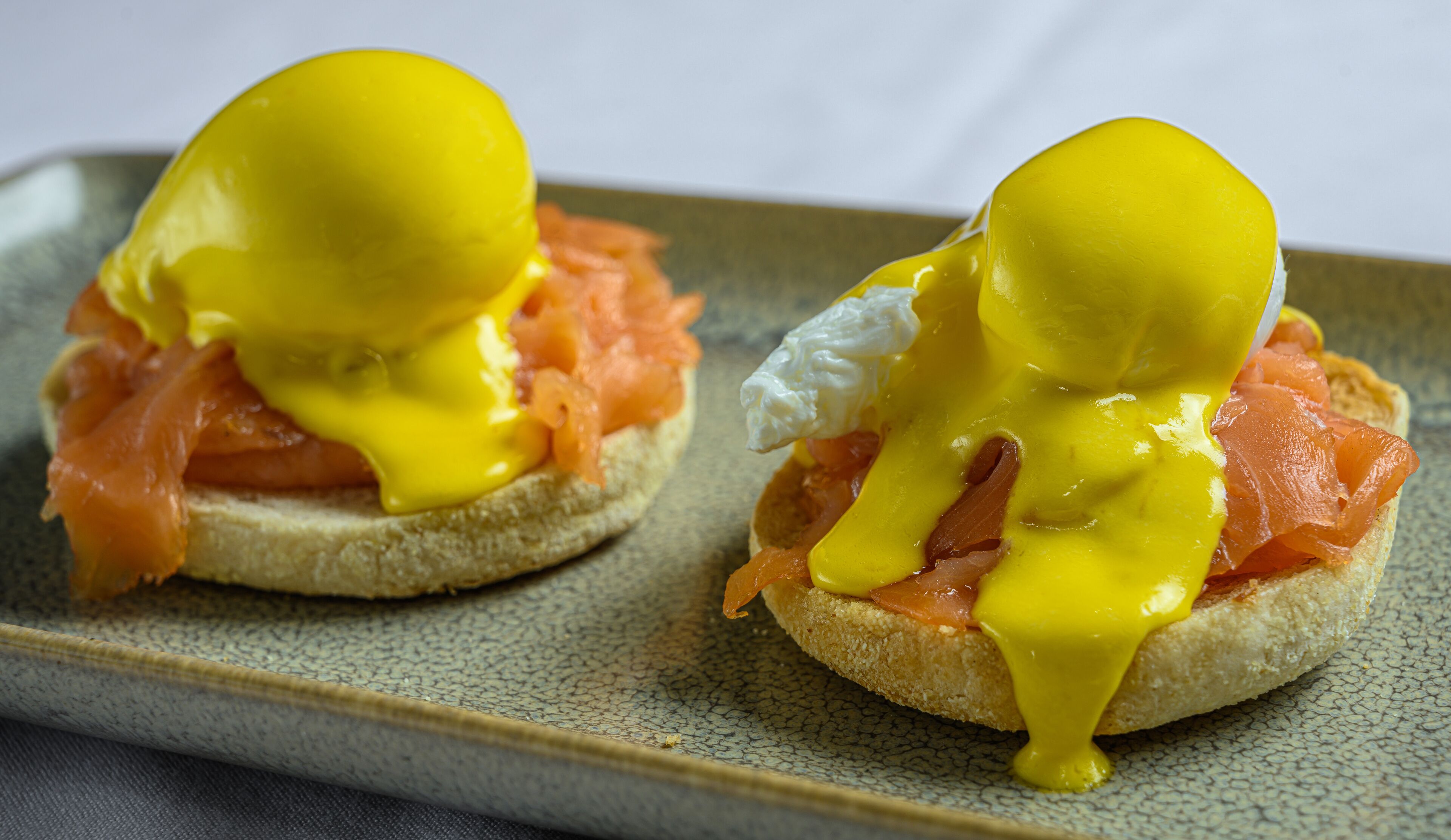 Two sandwiches with egg yolk and sauce on a textured plate.