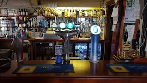 A bar with multiple taps, including Guinness and Theakston Best Bitter. There are shelves with various bottles and a sign for 'Fire exit'. - Ecclefechan Hotel (Lockerbie)