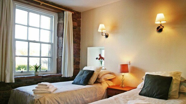 A hotel room with two beds, a large window, a stone wall, and two wall-mounted lamps. - Ecclefechan Hotel (Lockerbie)