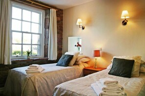 A hotel room with two beds, a large window, a stone wall, and two wall-mounted lamps. - Ecclefechan Hotel (Lockerbie)