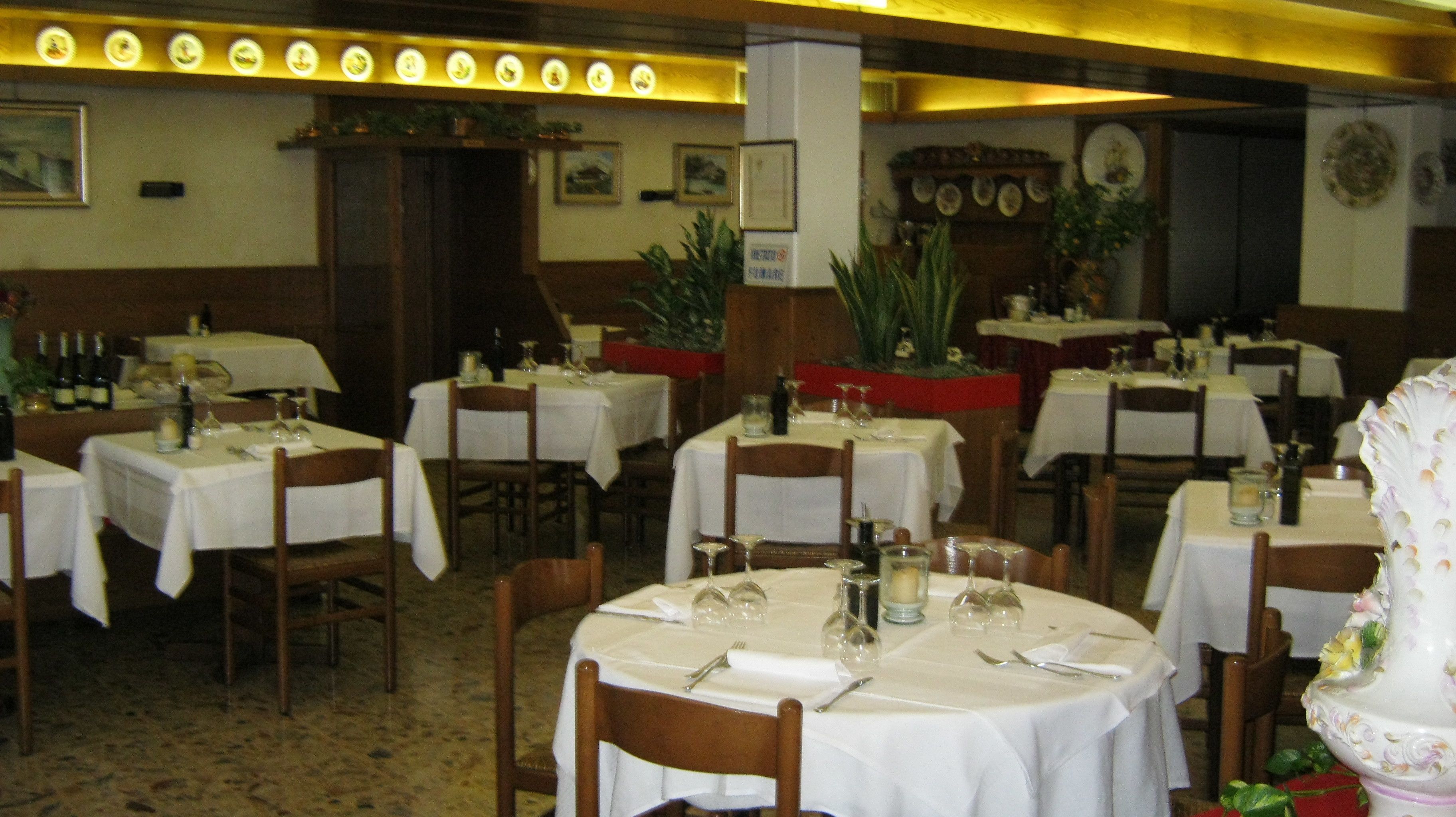 Un restaurante con varias mesas redondas dispuestas con manteles blancos, sillas y cubiertos.