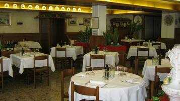 Un restaurante con varias mesas redondas dispuestas con manteles blancos, sillas y cubiertos.
