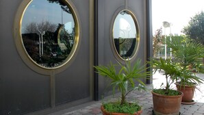 Fachada de edificio con dos espejos circulares grandes y plantas en macetas en el suelo.