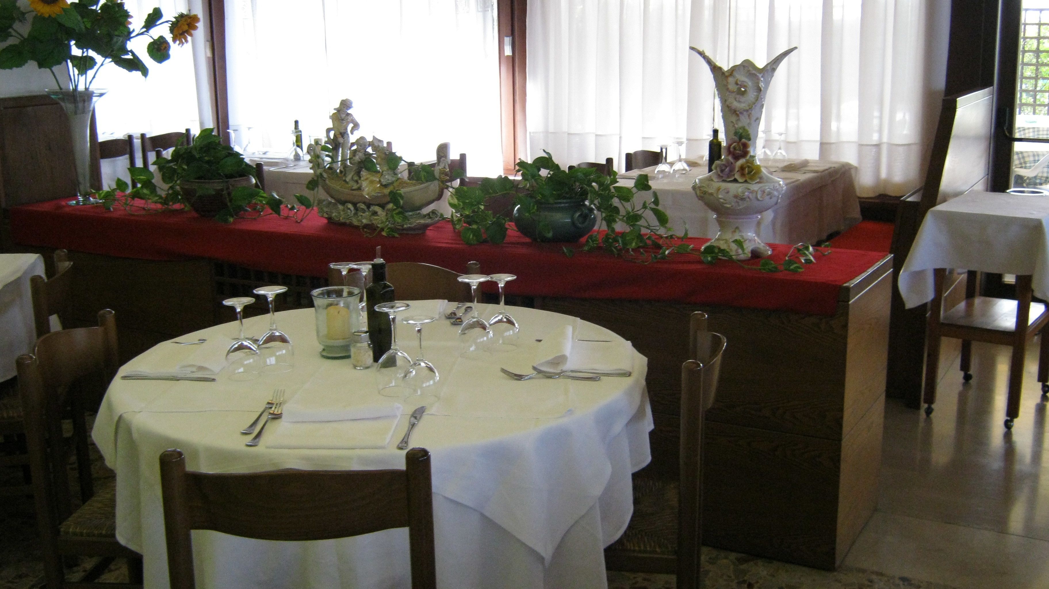 Un comedor con mesas redondas dispuestas para una comida, con cristalería transparente y un centro de mesa.