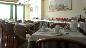 Un comedor con mesas dispuestas para el desayuno, sillas y un cuadro en la pared.