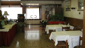 L’intérieur d’un restaurant, avec des tables dressées pour le service, une grande plante en pot et une porte donnant sur l’extérieur.