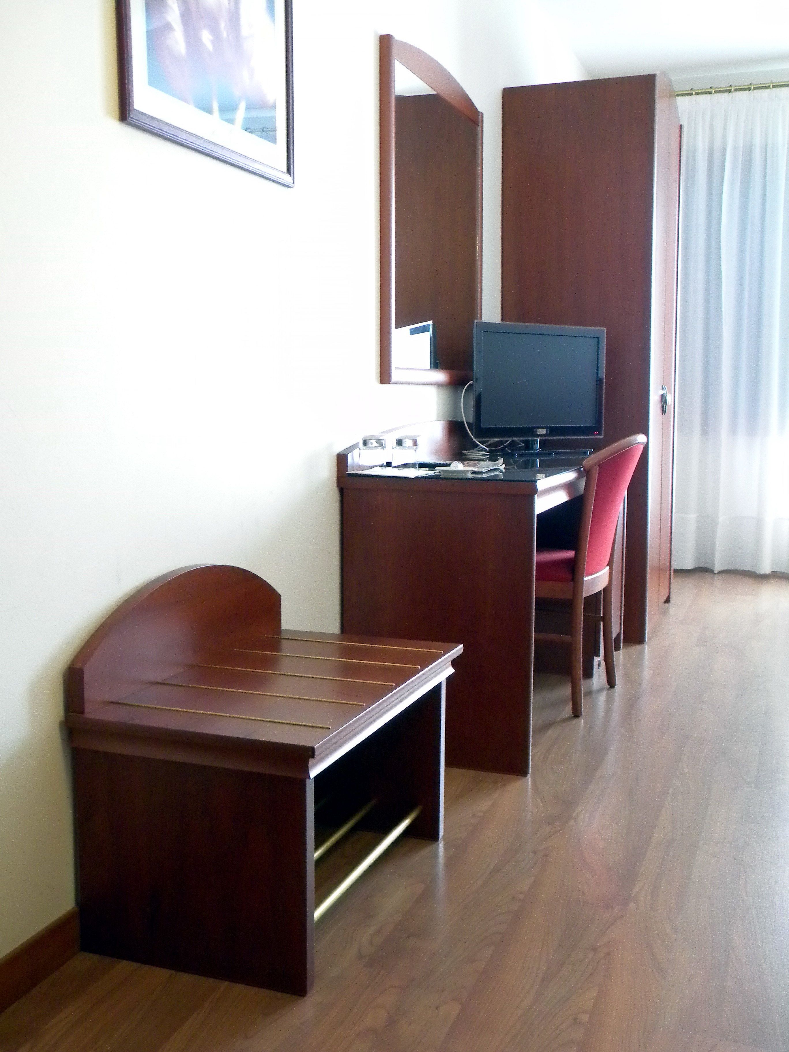 Una habitación de hotel compacta con un escritorio de madera, una silla, un televisor y una mesita.