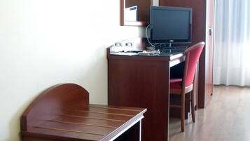 Una habitación de hotel compacta con un escritorio de madera, una silla, un televisor y una mesita.