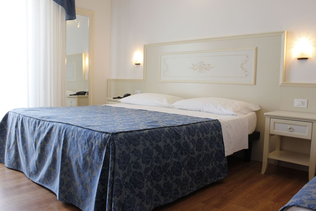 Une chambre d’hôtel avec un grand lit, une table de chevet avec une lampe, une commode et un luminaire fixé au mur.