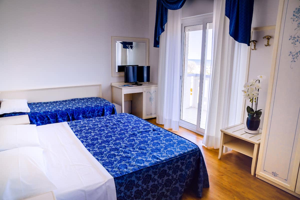 Une chambre d’hôtel avec deux lits, un bureau, un miroir, une plante en pot et une vue sur l’extérieur, visible à travers une porte vitrée.
