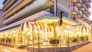 Un hôtel à plusieurs étages doté de balcons, d’une entrée couverte et d’un espace extérieur aménagé pour s’asseoir.