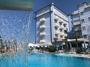 A hotel with a swimming pool, multiple balconies, and sun umbrellas. - Hotel Principe (Caorle)