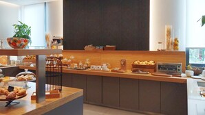 A modern breakfast bar with pastries, a coffee machine, and a plant.