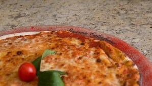 A pizza with a slice missing, garnished with a cherry tomato and basil leaf.