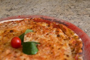 A pizza with a slice missing, garnished with a cherry tomato and basil leaf.