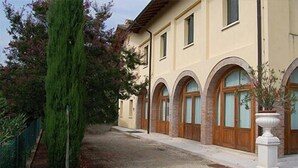 Un edificio con fachada color crema, ventanas arqueadas y un sendero de grava.